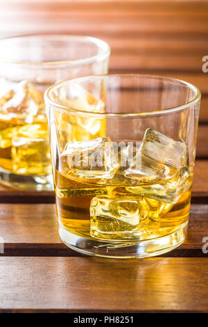Glass of alcoholic drink with ice cubes on wooden table. Whiskey in glass. Stock Photo