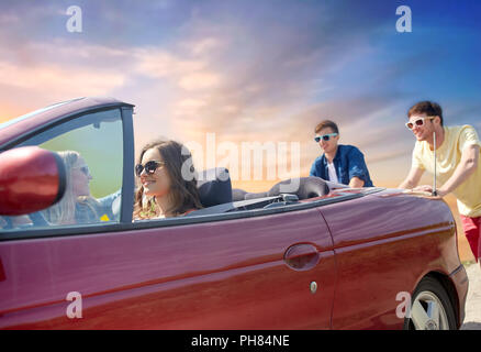 friends pushing broken convertible car Stock Photo