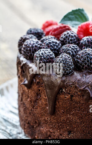 Close up homemade chocolate cake decorated with black and red raspberries on glass plate. Selective focus on berries Stock Photo