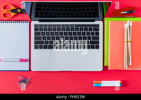 top view of laptop with blank screen and variety stationery on red background Stock Photo