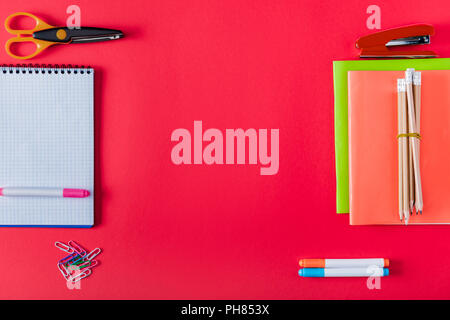 top view of arranged textbooks, stapler, markers, paper clips, scissors and blank notebook on red background Stock Photo