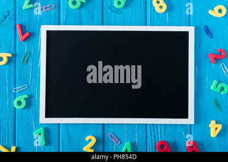 top view of empty blackboard, colorful numbers and paper clips on blue wooden background Stock Photo