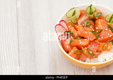 Hawaiian poke with salmon and sesame seeds, boiled rice, fresh cucumber, radish and green onions in porcelain bowl. Top view with copy space. Organic  Stock Photo