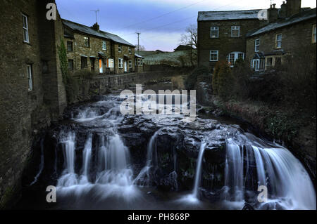 Evening descends on the houses beside Gayle Beck running though the centre of the village of Hawes in the Yorkshire Dales Stock Photo