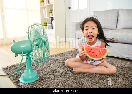 lovely girl laughing and holding a sliced melon. cross-legged sitting in front of a fan. feeling happy and cheerful. Stock Photo