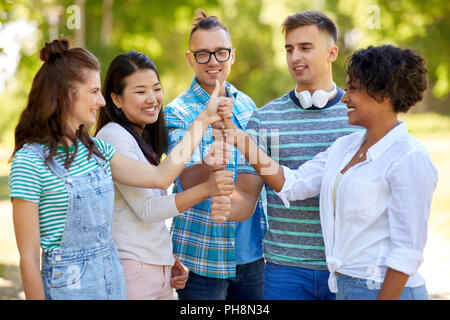 happy friends making thumbs up gesture in park Stock Photo