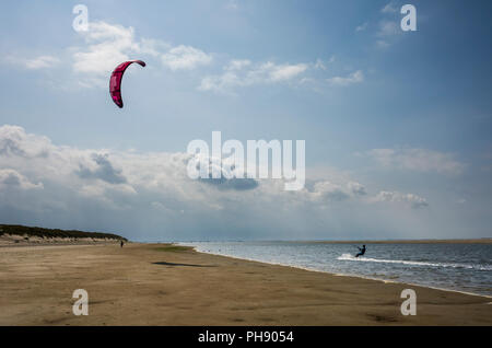 Am Strand Langeoog. Germany Deutschland.  A person is kitesurfing along the water's edge of the sandy beach.  A narrow strip of sea water stretches along the beach, which is idea for Watersport.  Photographed on a bright sunny day with mainly clear blue skies except for a few light clouds. Stock Photo