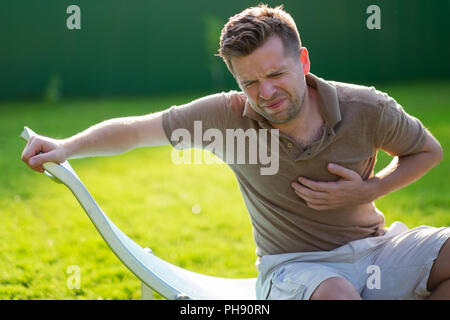 Young caucasain man having heart attack while sitting outdoor Stock Photo