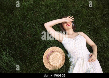 Top view of Pretty woman in dress and headphones lying on grass with closed eyes and listening music Stock Photo