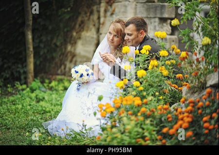 Newlyweds siting near flowers and holding hands Stock Photo