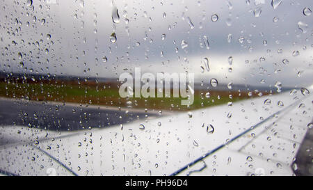 Raindrops on airplane window by the runway. Stock Photo