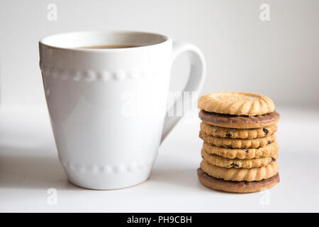 A cup of coffee in a white mug on a white background with a pile of biscuits stacked up next to the mug Stock Photo