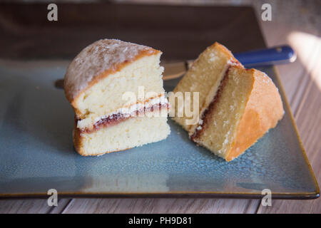 slices of Victoria Sponge cake sitting on a textured blue plate with a blue handled knife next to it. Stock Photo