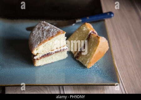 slices of Victoria Sponge cake sitting on a textured blue plate with a blue handled knife next to it. Stock Photo