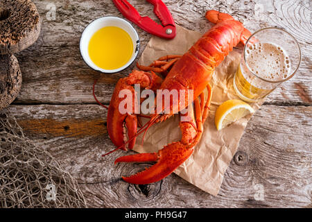 A delicious cooked atlantic lobster with melted butter, beer and lemon on a rustic wood background. Stock Photo