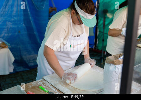 Woman wearing apron rolling out a dough with rolling pin at the street market in Krosno, Poland during the Carpathian Climates festival Stock Photo