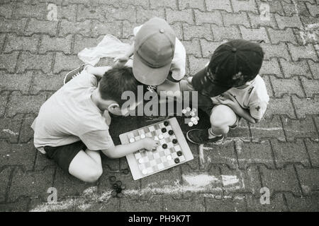 Three boys playing checkers board game outdoors. Stock Photo