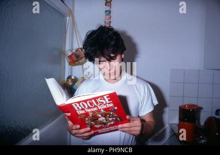 Sänger Nino de Angelo studiert ein Kochbuch von Paul Bocuse in einer Homestory Fotoreportage in Köln, Deutschland 1983. Singer Nino de Angelo reading  Stock Photo