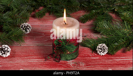 Burning candle on rustic red wooden boards with Christmas decorations Stock Photo