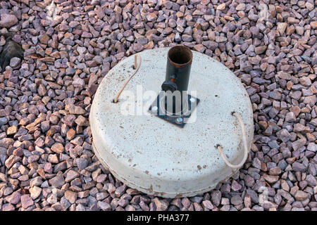 A concrete umbrella stand ontop of small stones in the garden Stock Photo