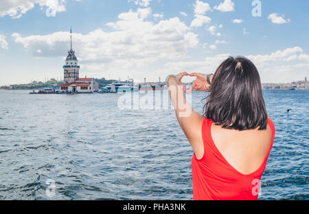 Beautiful Chinese woman makes heart shape with hands on view of Maidens Tower,a popular destination in Istanbul,Turkey. Stock Photo