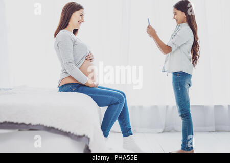 Cute little daughter photographing her adorable pregnant mother Stock Photo