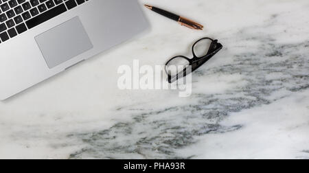 Marble desktop setting with laptop with pen and reading glasses Stock Photo