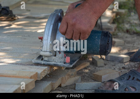 Electric circular saw is being cut a piece of wood by carpenter. Construction details of male worker close-up. Formwork for the fence. Stock Photo
