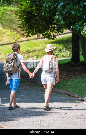 Tourists couple with backpacks walking along a road on a summer trip. Stock Photo