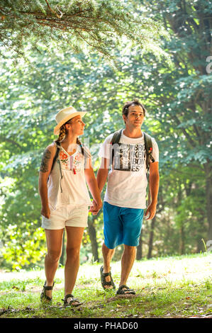 Tourists couple with backpacks walking along a road on a summer trip. Stock Photo