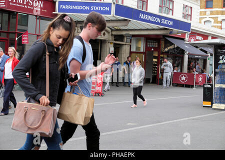 A young woman couple with shopping bags handbag and mobile phone walking in street outside Farringdon Station in Clerkenwell, London UK   KATHY DEWITT Stock Photo