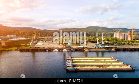 Aerial photo of  harbor cranes and  and barge with sand  over  river harbor landscape located in  industrial background. Aerial view:Barge with cargo  Stock Photo