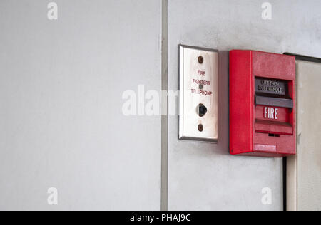 Push button switch, fire alarm on grey wall for alarm and security system with fire extinguisher port. Stock Photo