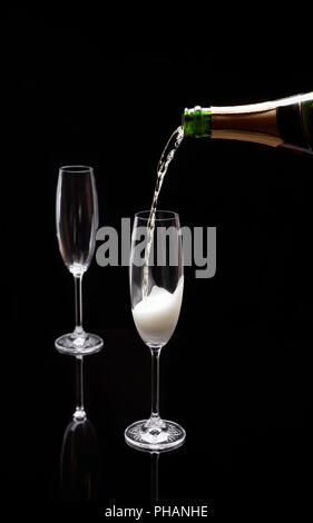 A bottle pouring champagne into one of two champagne flutes on a black background Stock Photo