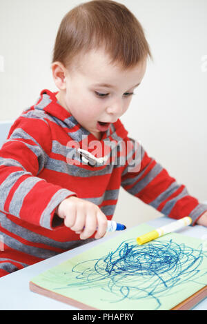 Portrait of cute Caucasian white little boy toddler drawing with color pencils markers on paper in album, looking surprised, excited, mouth open in ex Stock Photo