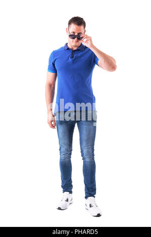 Serious confident young casual man holding sunglasses with over the glasses look at camera. Full body isolated on white background. Stock Photo