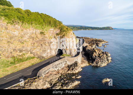 Causeway Coastal Route with Black Arc tunnel. Scenic road along eastern coast of County Antrim, Northern Ireland, UK. Aerial view in sunrise light