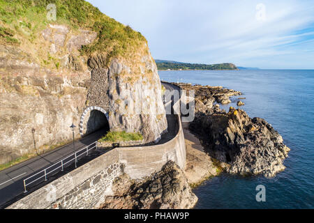 Causeway Coastal Route with Black Arc tunnel. Scenic road along eastern coast of County Antrim, Northern Ireland, UK. Aerial view in sunrise light