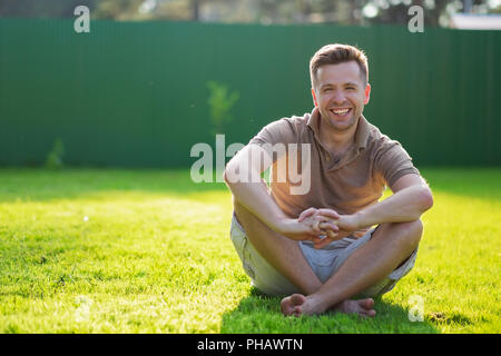 Young happy man smiling at camera sitting on the green grass Stock Photo