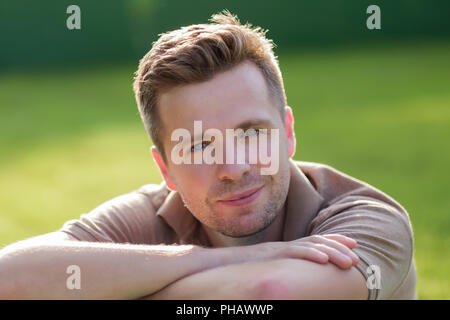 Young happy man smiling at camera sitting on the green grass Stock Photo
