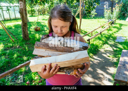 little girl hand hold wooden logs, an armful of firewood. Stock Photo