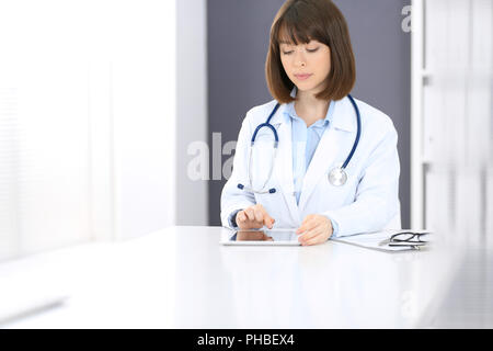Doctor typing on laptop computer while sitting at the white table in hospital office. Physician at work. Medicine and healthcare concept. Stock Photo