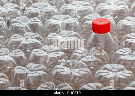 Single unique plastic bottle with red cap amongst many upturned clean empty bottles in a concept of recycling and individuality, full frame close up v Stock Photo