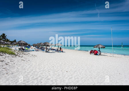 Varadero, Cuba / March 17, 2016: Resort guests enjoying shade of grass topped umbrellas at the beach. Stock Photo