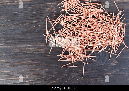copper finish nails lying in a pile, close-up of metal materials used in construction, top view on a blackboard background Stock Photo
