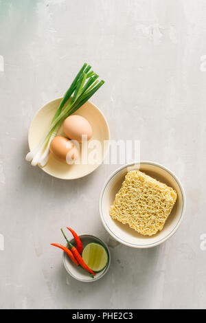 Instant noodles in bowl and vegetable side dishes on stone background. Quick & easy food concept. Stock Photo