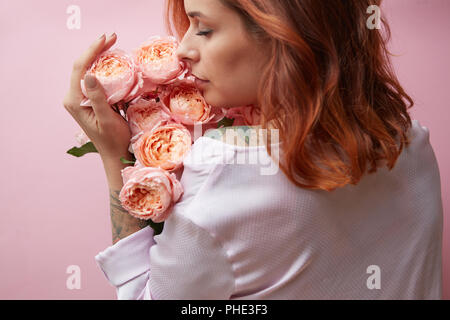 Cute woman is sniffing a bouquet of pink roses Stock Photo