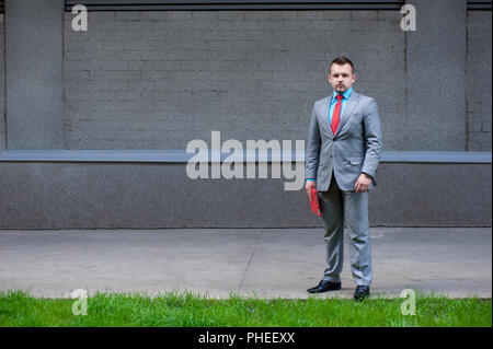 Young male in formal wear with red gadget and tie at urban background Stock Photo