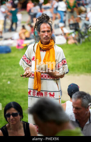 Young new age hippie man surrounded by people holds a mortar and pestle grinder in his hands in Mount Royal Park, Montreal, Canada. Stock Photo