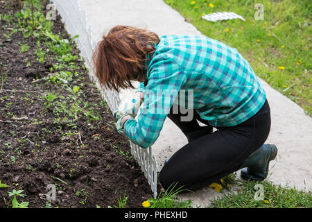 Woman fixing a decorative fence on a flower bed Stock Photo